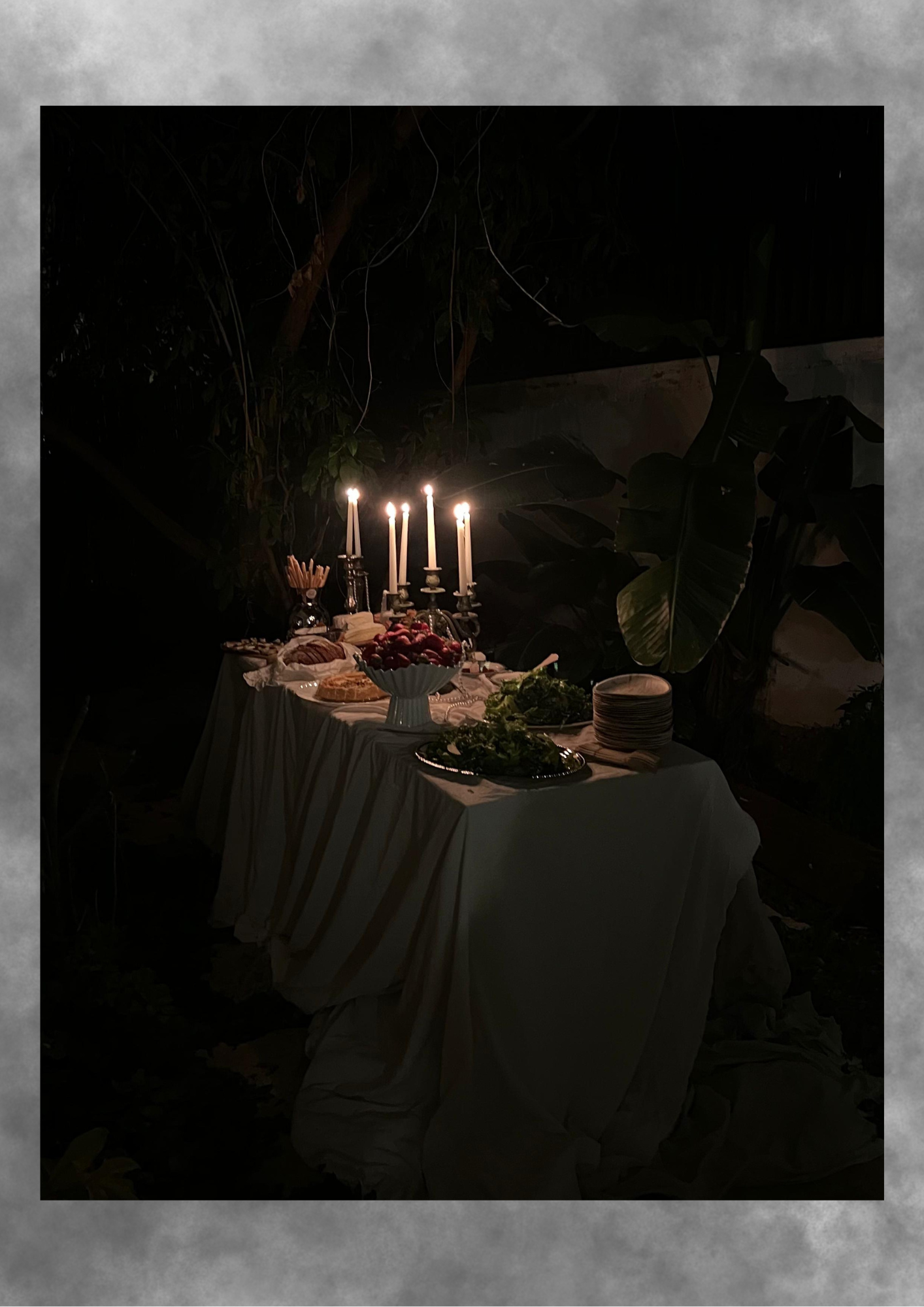 Nighttime candlelit table arranged beneath dense foliage.