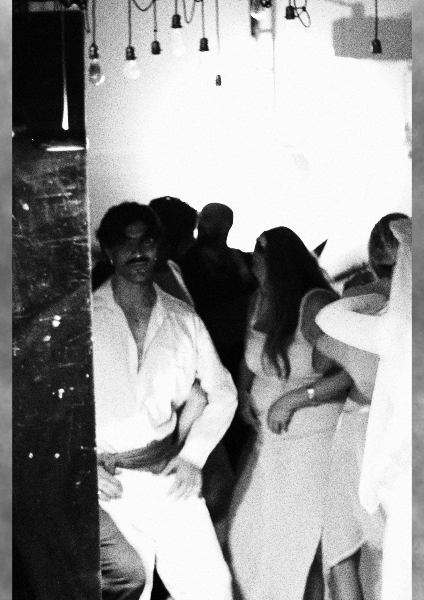 Guests in white garments gathered indoors in grainy black and white.